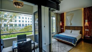 A hotel room with a bed, a table with chairs, a window with a view of buildings, and a balcony. - Warwick Centre (Nairobi)