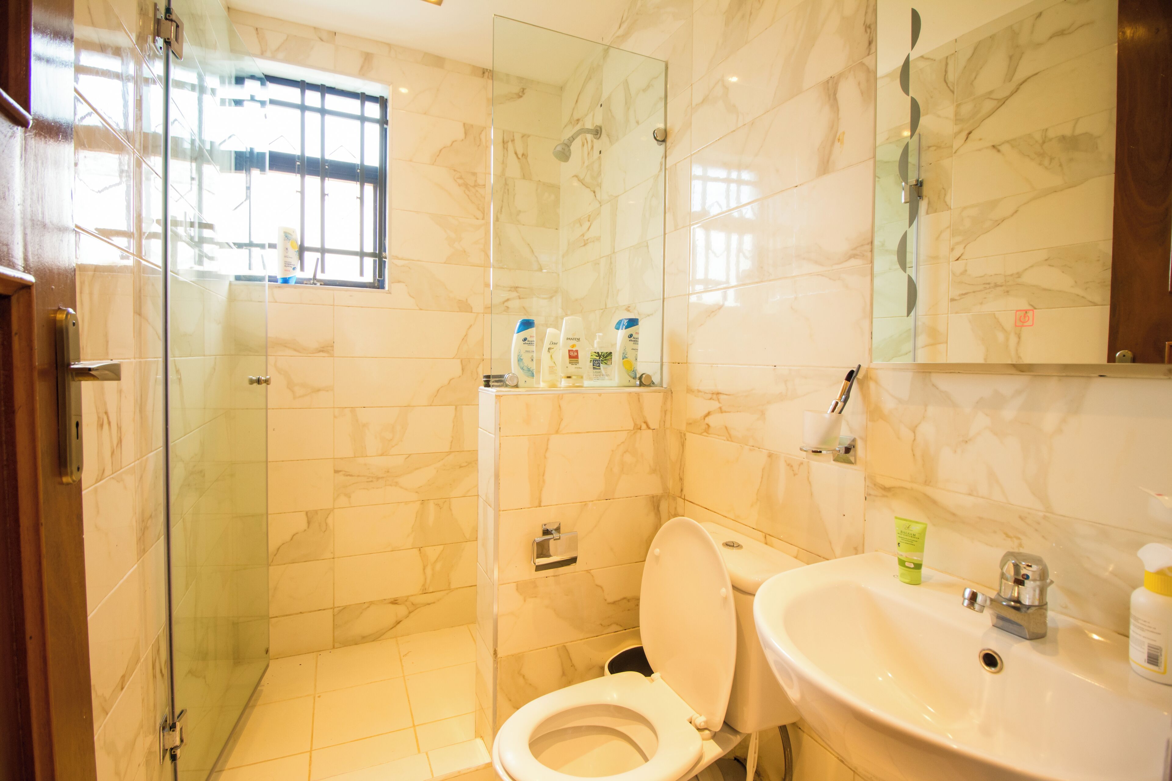 Un baño con ducha de vidrio, inodoro y lavamanos con artículos de aseo.