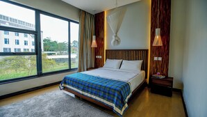 A modern hotel room with a large window, a bed with a plaid bedspread, wooden headboard, and two bedside lamps. - Warwick Centre (Nairobi)