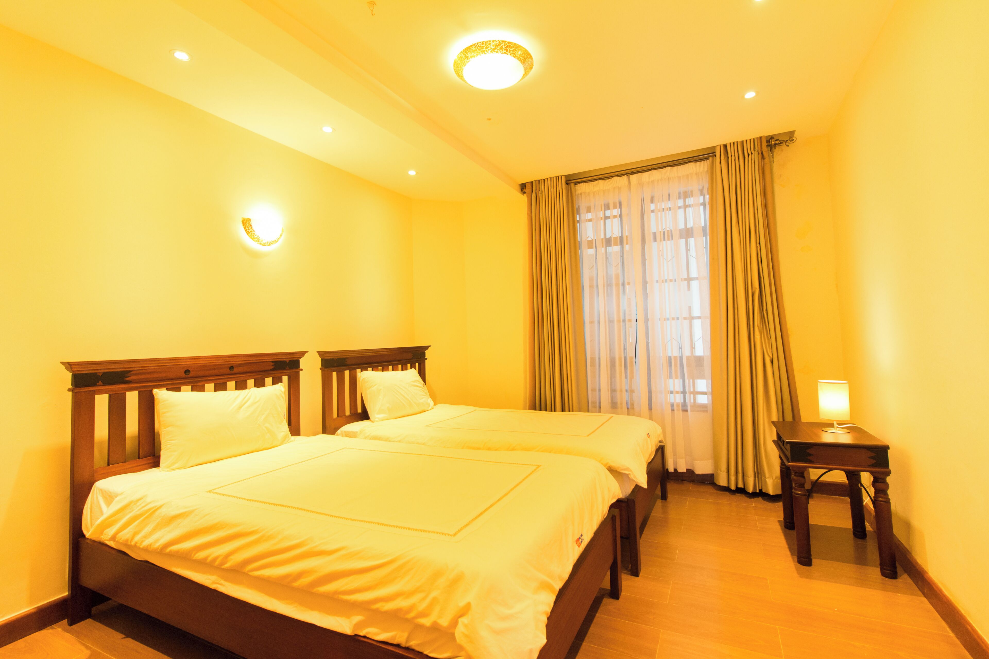 A hotel room with two beds, a bedside table, and a window with curtains.