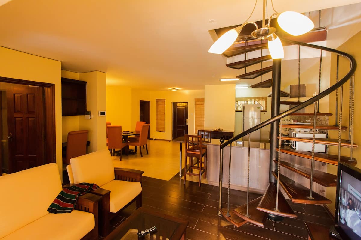 Uma sala de estar moderna com uma escada curva, uma área de jantar e uma cozinha ao fundo.
