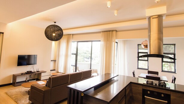 A modern living room with a sofa, a flat-screen TV, a dining area, and a kitchen with a large island. - Warwick Centre (Nairobi)