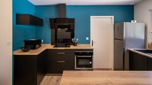 Une cuisine moderne avec un mur d’accent bleu, des meubles de cuisine noirs, un four encastré et un réfrigérateur en acier inoxydable.