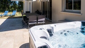 Un bain à remous avec une table et des chaises à proximité, un patio couvert et une porte-fenêtre coulissante donnant sur un espace extérieur.