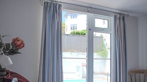 Un dormitori amb llit, una taula de nit amb làmpada, finestra amb cortines i vista a una piscina i un edifici a l'exterior.