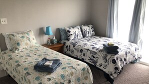 A bedroom with two single beds, each with floral-patterned bedding, a nightstand with a lamp, and a window with curtains. - Bay View Bungalow by the Pier - Swimming Pool and Pet Friendly - 30 Day Listing (Norfolk)