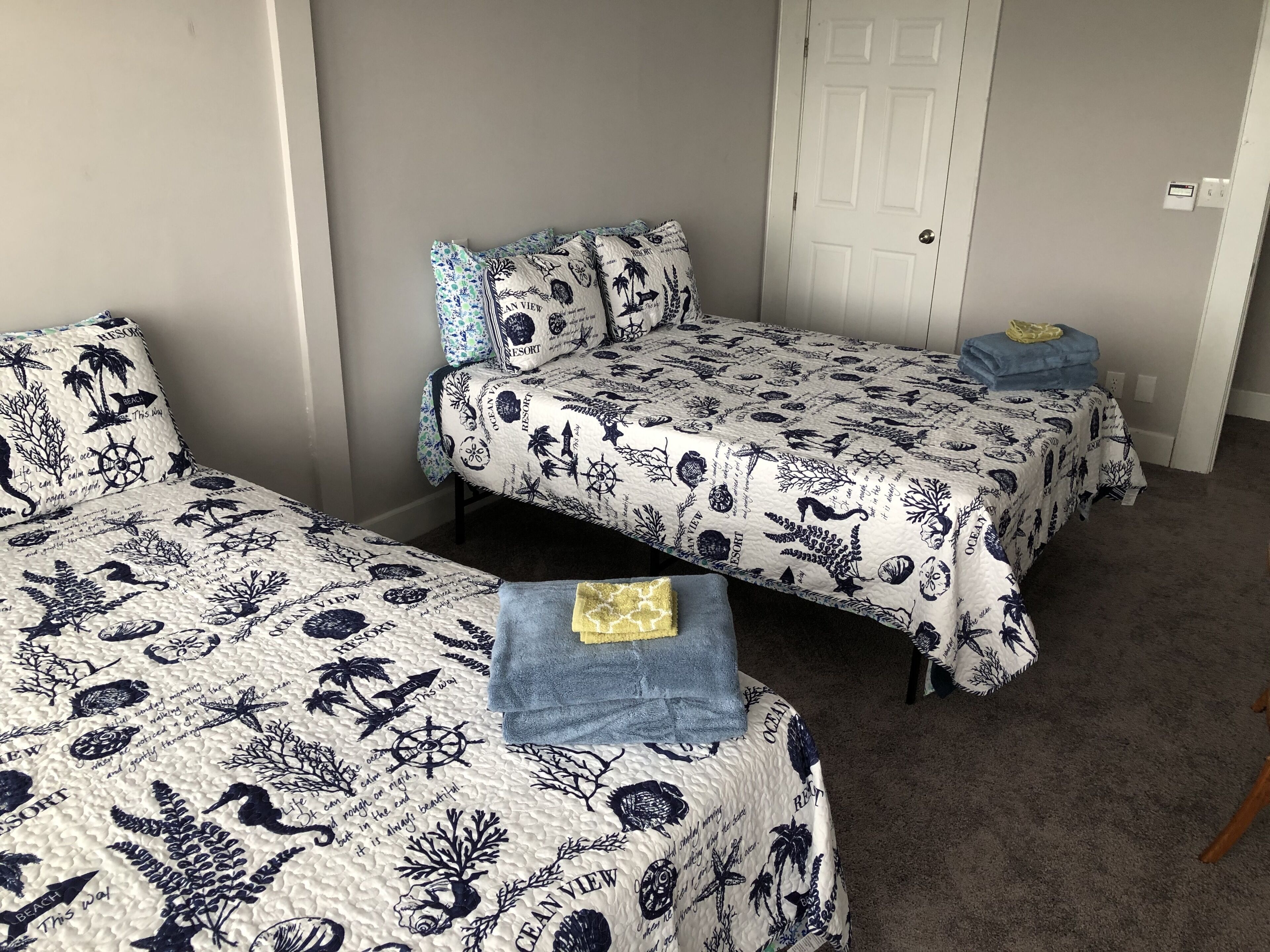 A room with two single beds, each with a patterned bedspread and matching pillows. There are two small bedside tables with towels.