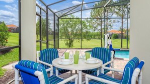 A covered patio with a table set for four, surrounded by striped chairs, overlooking a swimming pool and a grassy area.
