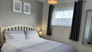A neatly made bed with striped bedding, a bedside lamp, and two framed pictures on the wall. - M & T Chalets , Detached Modern 2 bed Chalet, Sleeps 6 (Hemsby)