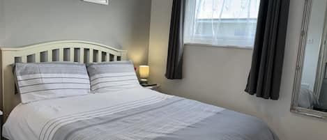 A neatly made bed with striped bedding, a bedside lamp, and two framed pictures on the wall.