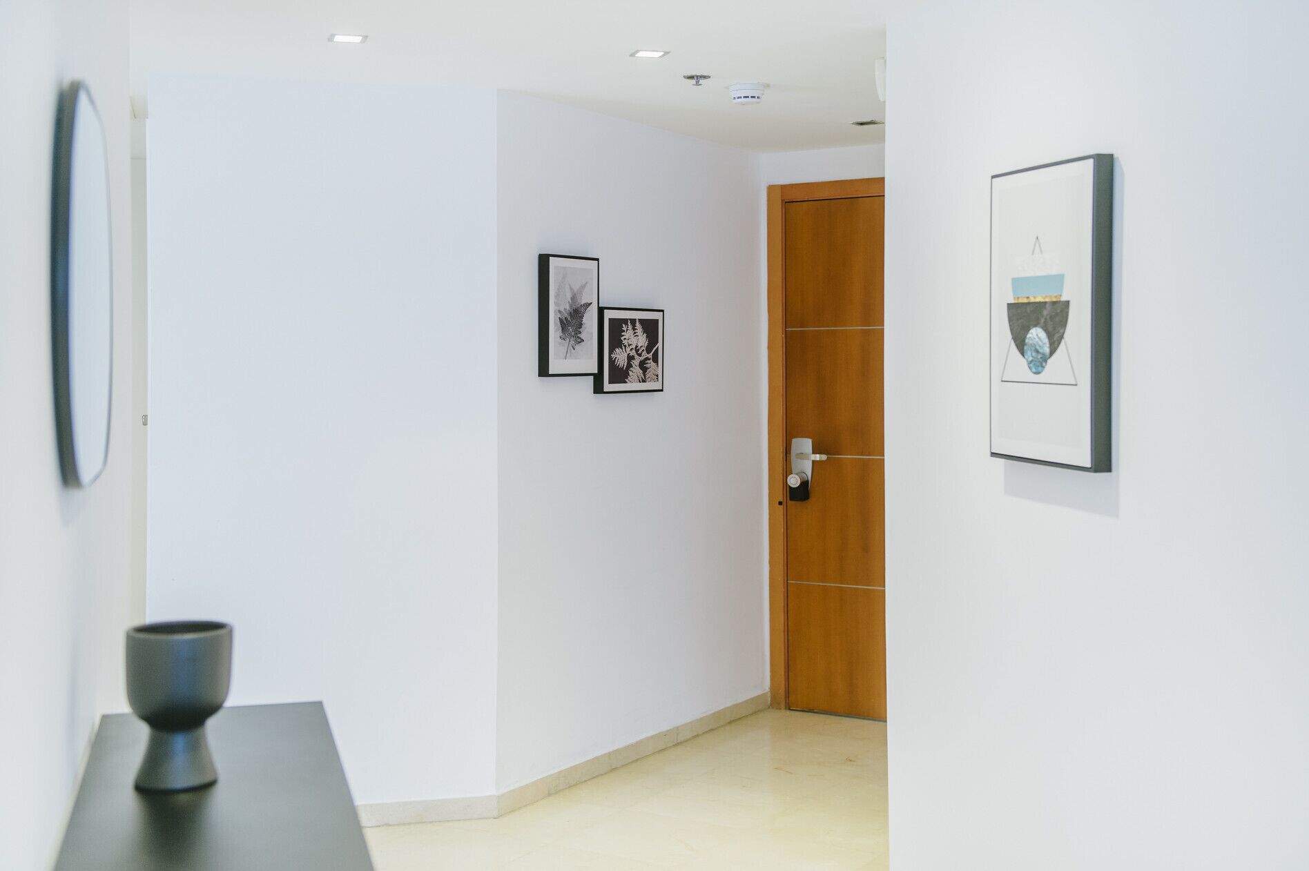 A hallway with white walls, a wooden door, and framed artwork.