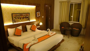 A hotel room with a large bed, two chairs, a small table, a picture on the wall, and a window with curtains. - Hotel Agnija  (Udaipur)
