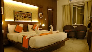 A hotel room with a large bed, a wall-mounted painting, a small table, and wicker chairs. - Hotel Agnija  (Udaipur)