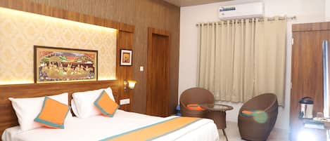 A hotel room with a bed, a ceiling fan, a wall-mounted air conditioner, a wicker chair, and a small table.