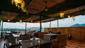 An outdoor dining area with wicker furniture, hanging lights, and a view of the landscape. - Hotel Agnija  (Udaipur)