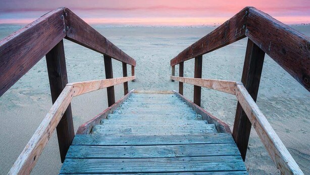 Una passera de fusta que condueix a una platja amb un cel ocre al fons.