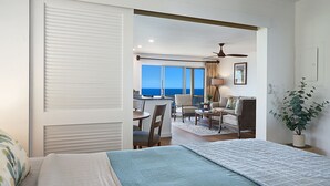 A bedroom with a bed, a view of the ocean, a dining area with chairs, and a ceiling fan. - Direct Ocean Front - Renovation Complete  - EVERYTHING inside is NEW! (Koloa)