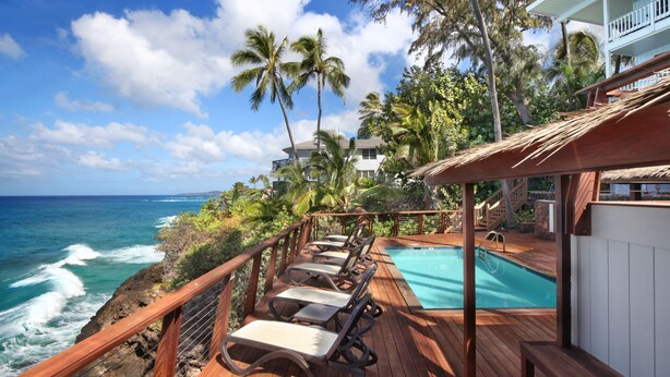 A wooden deck with lounge chairs overlooking a swimming pool and ocean waves. - Direct Ocean Front - Renovation Complete  - EVERYTHING inside is NEW! (Koloa)