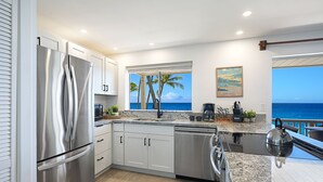 A modern kitchen with stainless steel appliances, a large window with a view of the ocean, and a dining area with a view of the sea. - Direct Ocean Front - Renovation Complete  - EVERYTHING inside is NEW! (Koloa)