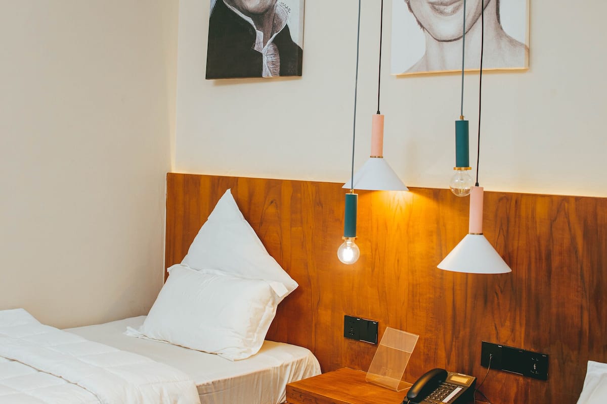 Une chambre d’hôtel avec deux lits, une tête de lit en bois, des tables de chevet avec des lampes et des œuvres d’art accrochées au mur.