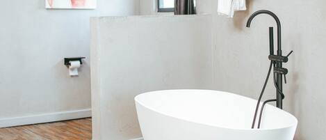 A modern bathroom with a freestanding bathtub, a window with curtains, a towel rack, and a toilet paper holder.