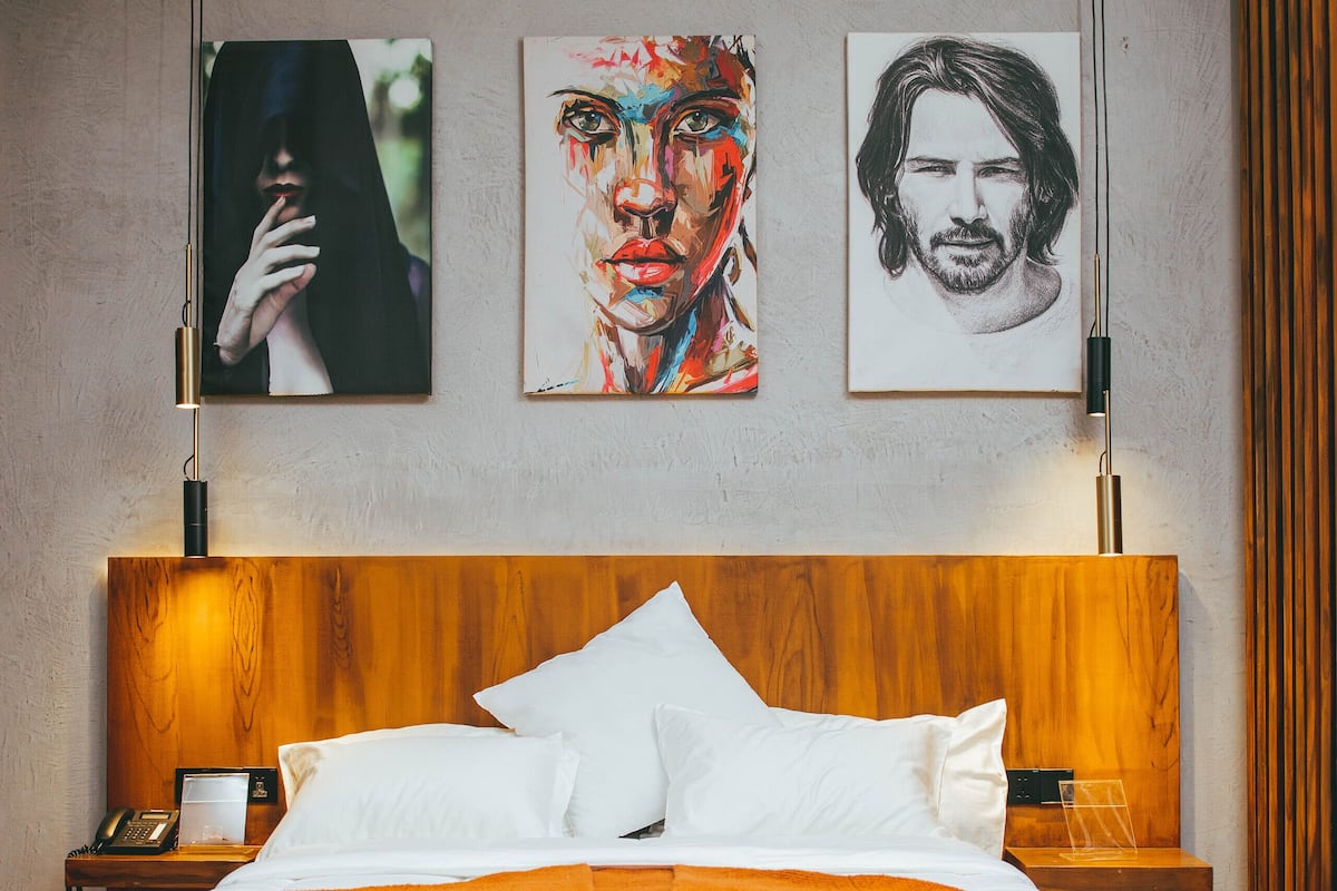 Une chambre à coucher moderne avec une tête de lit en bois, du linge de lit blanc et trois œuvres d’art encadrées accrochées au mur.
