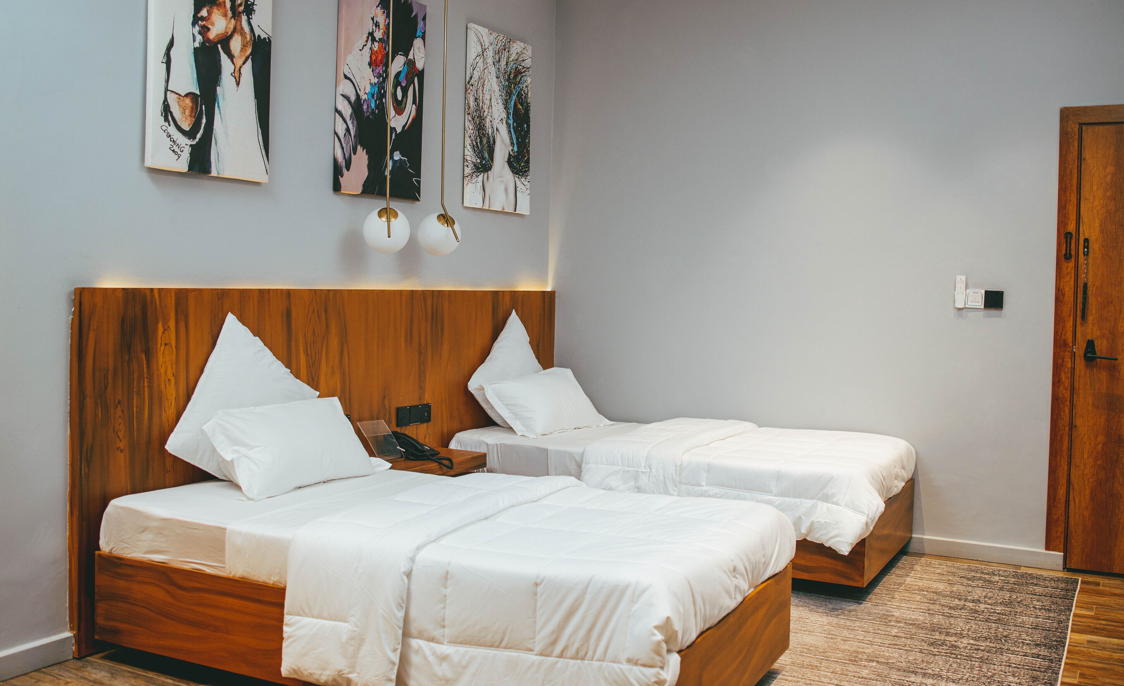 A hotel room with two beds, wooden headboards, white bedding, and artwork on the wall.