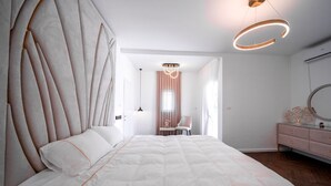 A modern bedroom with a large bed, a vanity with a mirror, and a chandelier.