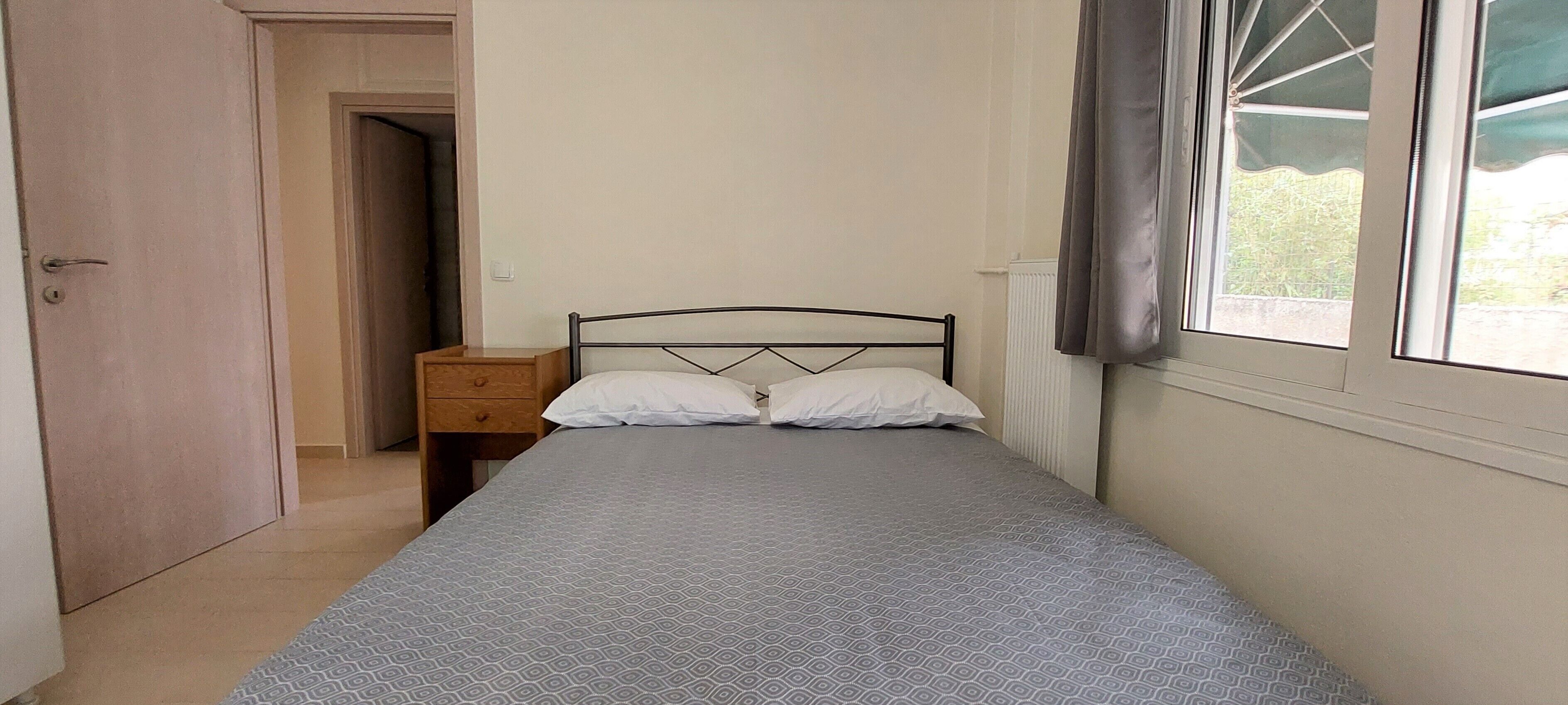 A bedroom with a bed, a nightstand, a wooden wardrobe, and a window with curtains.
