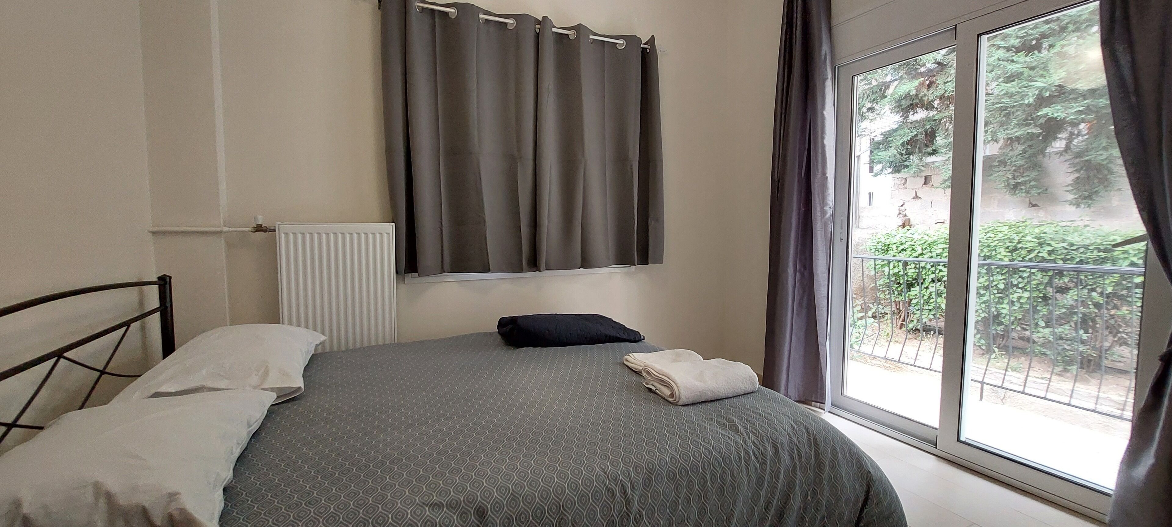 Une chambre à coucher avec un lit, une fenêtre avec des rideaux, un radiateur et une vue sur la verdure à l’extérieur.