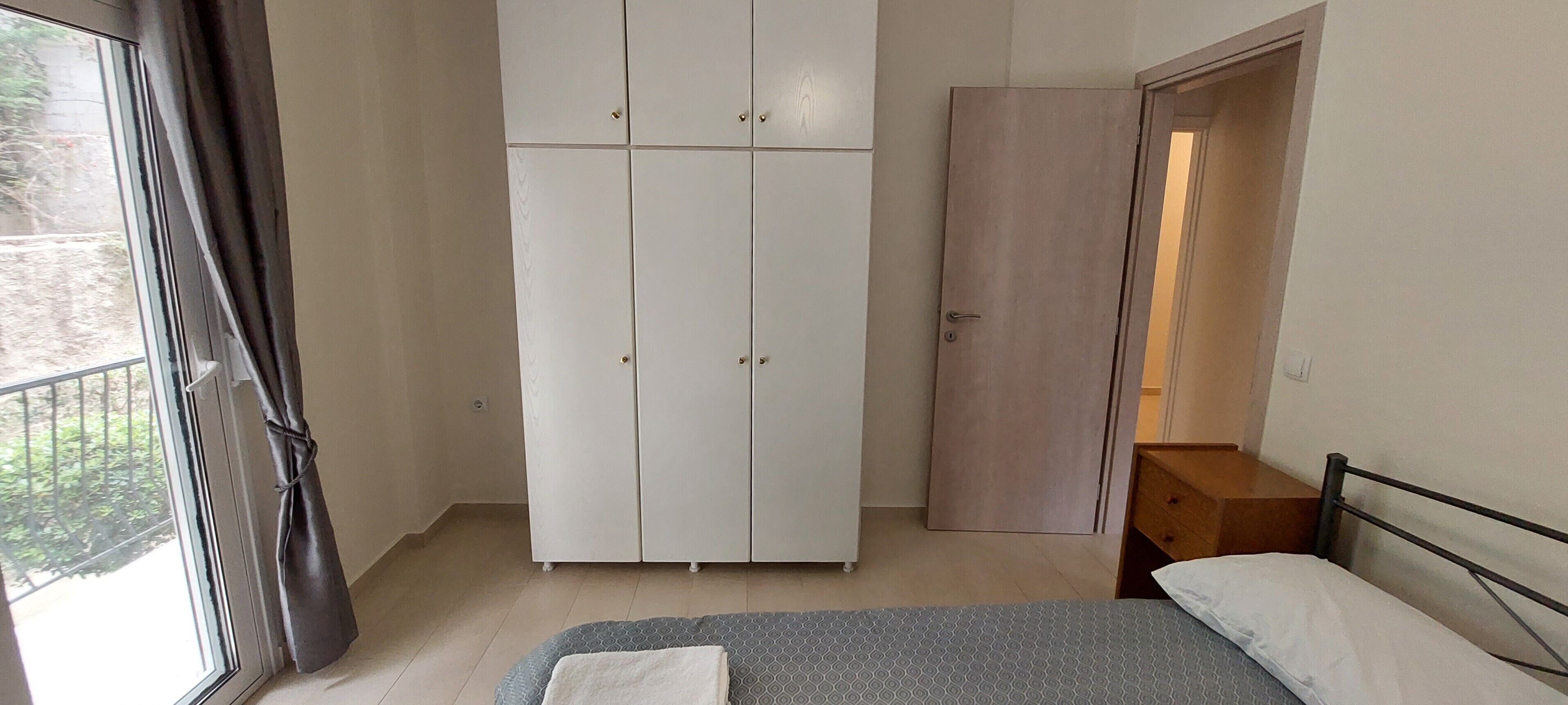 Une chambre à coucher avec un lit, une armoire, une porte en bois et une fenêtre avec des rideaux.