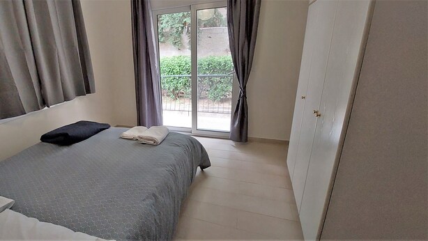 Ein Schlafzimmer mit Bett, Heizkörper, Fenster mit Vorhängen und Kleiderschrank.