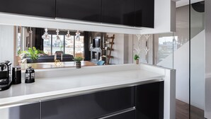 Eine moderne Küche mit schwarzen Schränken, einer weißen Arbeitsplatte und Blick in den Wohnbereich durch eine offene Tür.