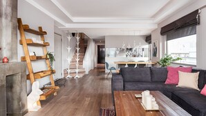 Ein modernes Wohnzimmer mit einer schwarzen Couch, einer Holzleiter und einer Treppe, die in eine Küche führt.