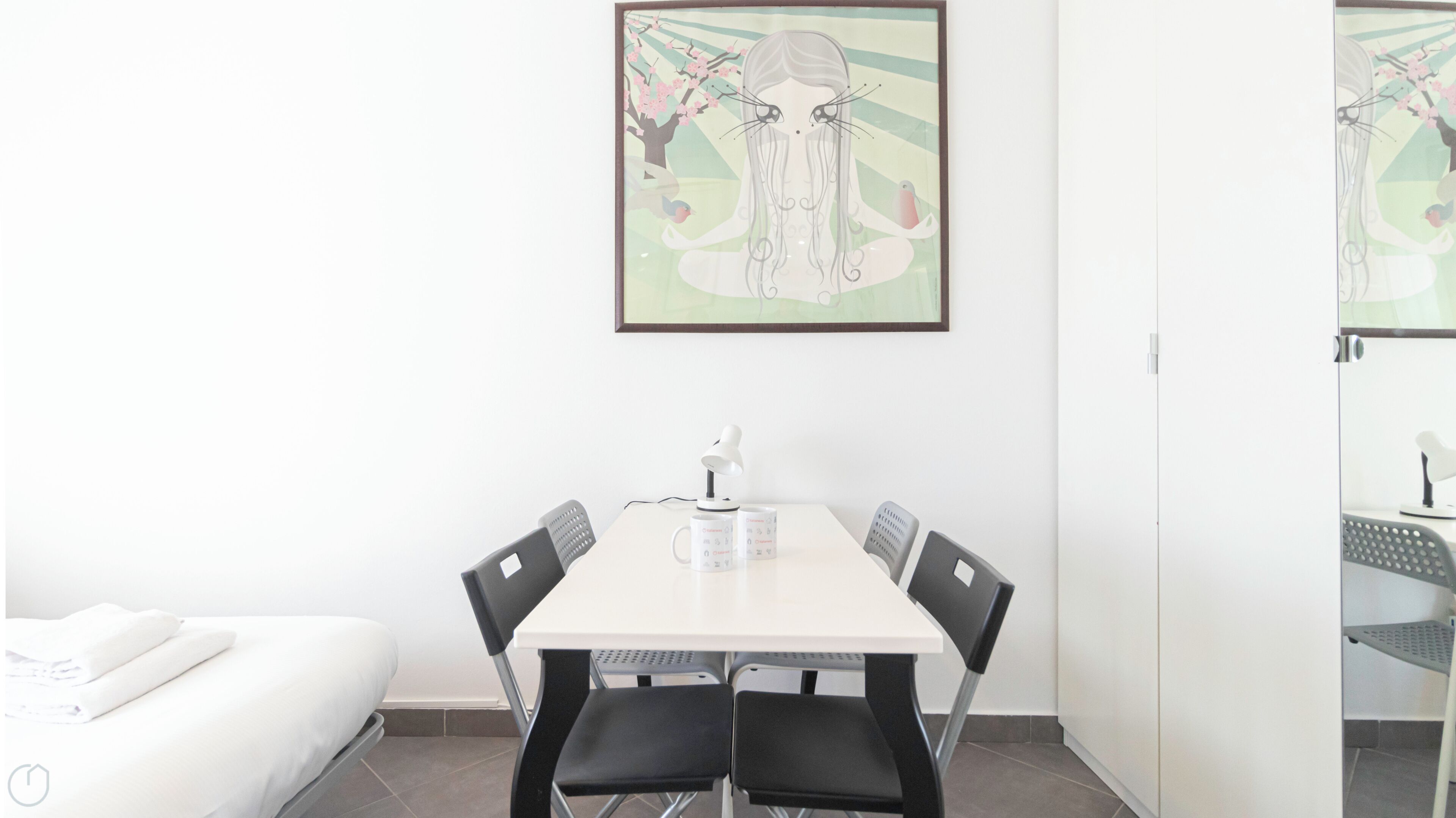 Une chambre d’hôtel moderne avec un lit blanc, une table à manger avec des chaises, un bureau blanc avec une lampe et une œuvre d’art encadrée accrochée au mur.