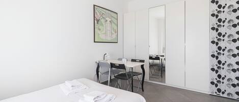A hotel room with a bed, a desk with a chair, a whiteboard, and a wardrobe.