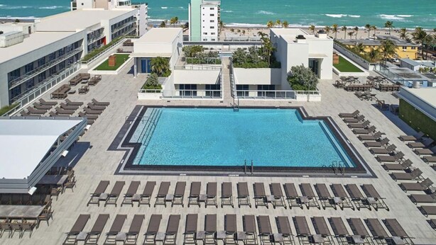 A rooftop pool with lounge chairs, a view of the ocean, and modern buildings. - Costa Hollywood Beach Studios (Hollywood)