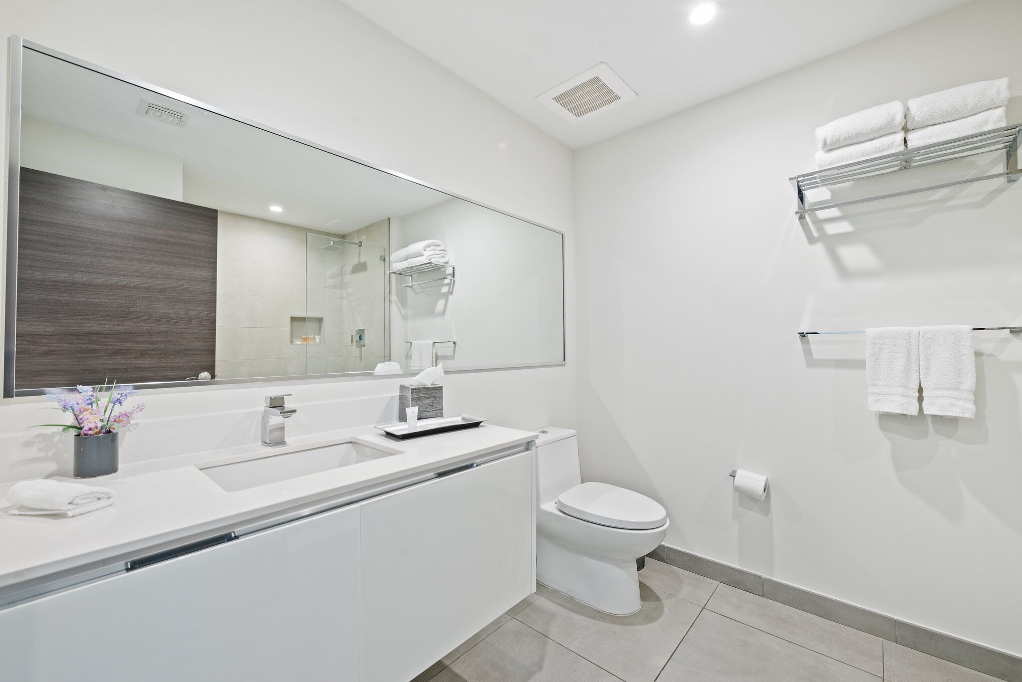 A modern bathroom with a large mirror, white fixtures, and neatly arranged towels.