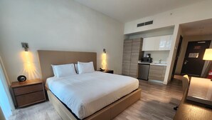 A modern hotel room with a large bed, bedside tables, a built-in desk, and a kitchenette area. - Costa Hollywood Beach Studios (Hollywood)