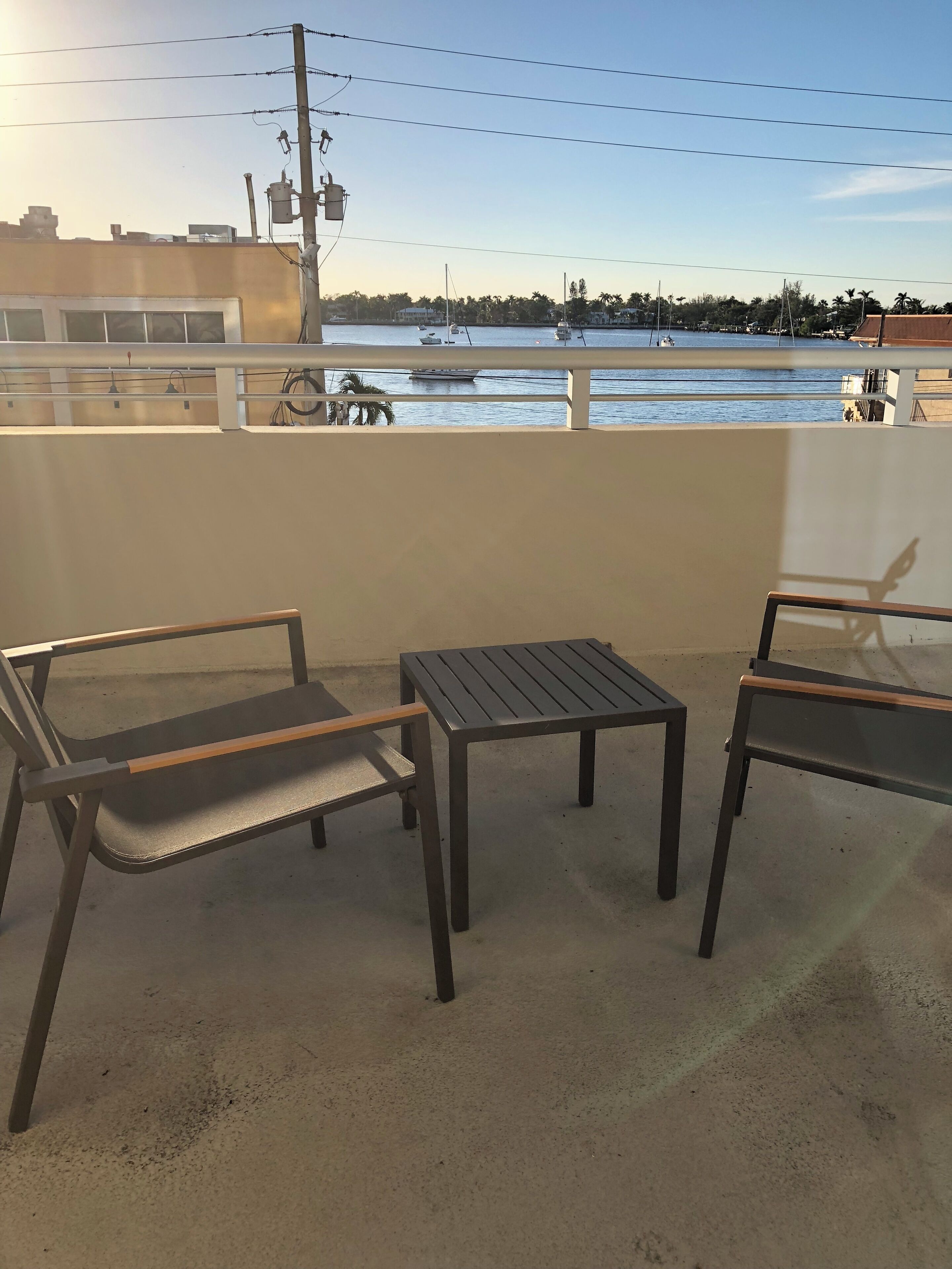 A balcony with two chairs and a table, overlooking a body of water with boats and buildings in the background.
