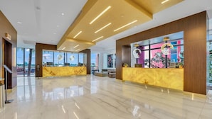 A spacious lobby with a marble floor, two reception desks with yellow marble tops, and large windows offering a view of the outside. - Costa Hollywood Beach Studios (Hollywood)