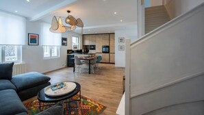 Een moderne woonkamer met een bank, salontafel en een kleurrijk vloerkleed. Een trap leidt naar een verdieping erboven.