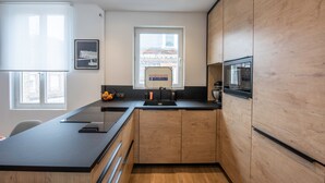 Een moderne keuken met een zwart aanrecht, houten kastjes, een inbouwoven en een raam met uitzicht op de stad.