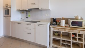 Una cuina moderna amb armaris blancs, forn integrat, un rentaplat i un moble lateral de fusta amb calaixos d'emmagatzematge.