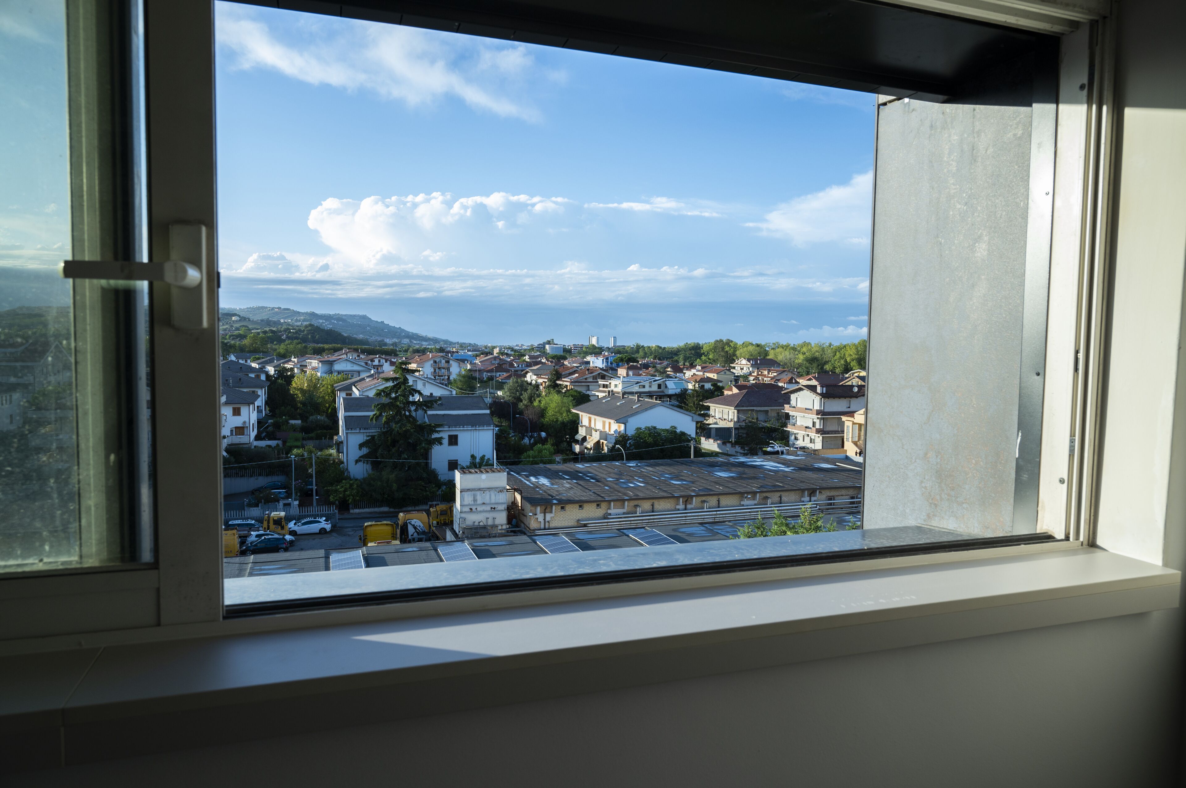 Une vue depuis une fenêtre donnant sur un quartier résidentiel, avec des maisons et un ciel dégagé.
