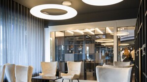 Un interior moderno con una zona de estar que incluye sillones blancos y una mesa de mármol, iluminación circular en el techo y vistas a un comedor.