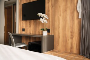 Una habitación de hotel moderna con una pared de madera, un televisor de pantalla plana, un escritorio con una silla y una orquídea en maceta.