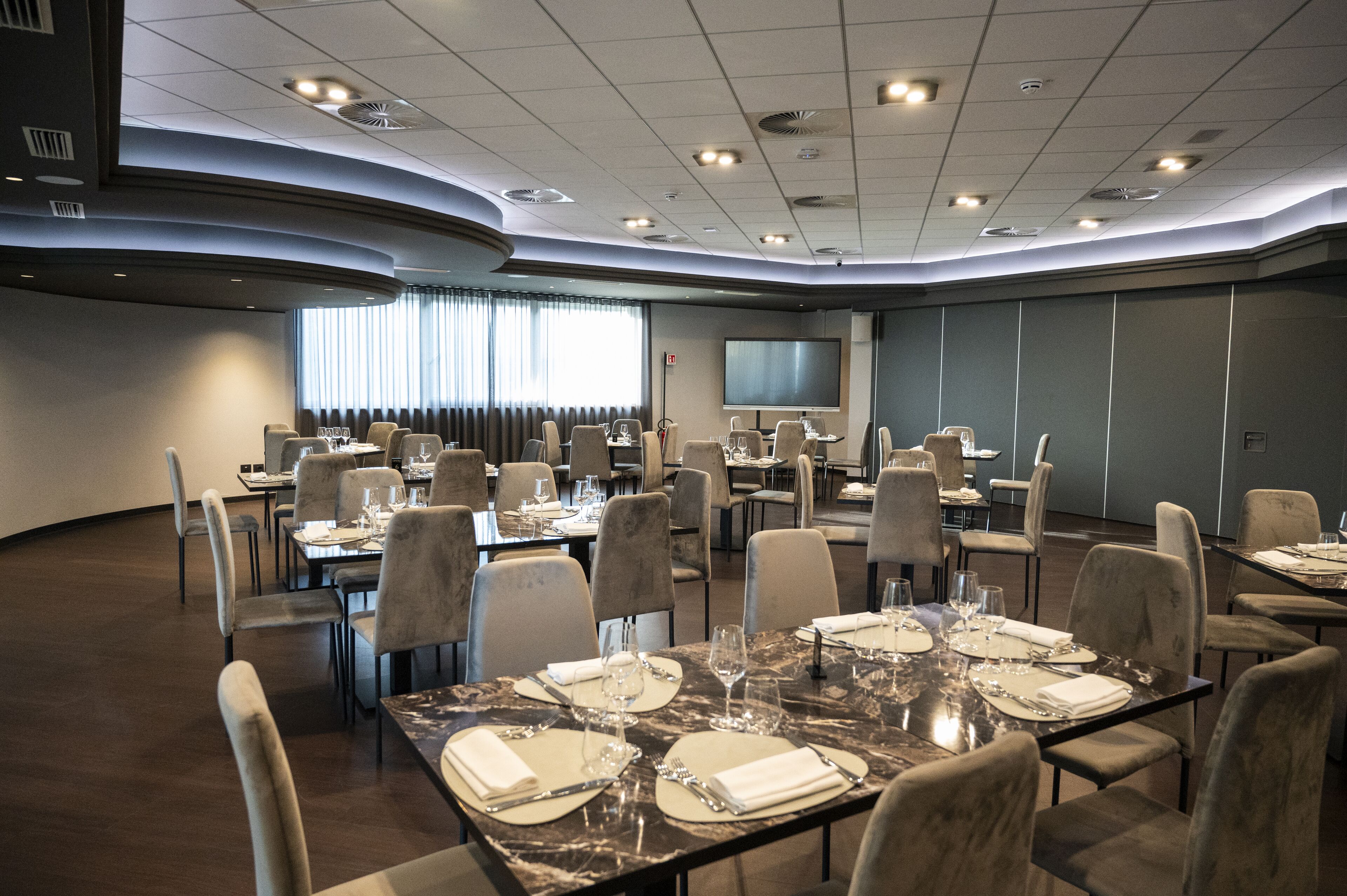 A conference room with multiple tables set for dining, equipped with chairs, and a large screen.