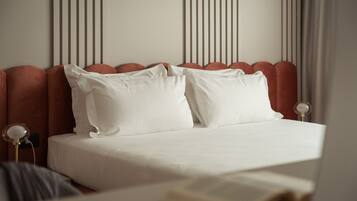 Una cama bien tendida con sábanas blancas y dos almohadas, una mesita de noche con lámpara, y una pared con líneas verticales.