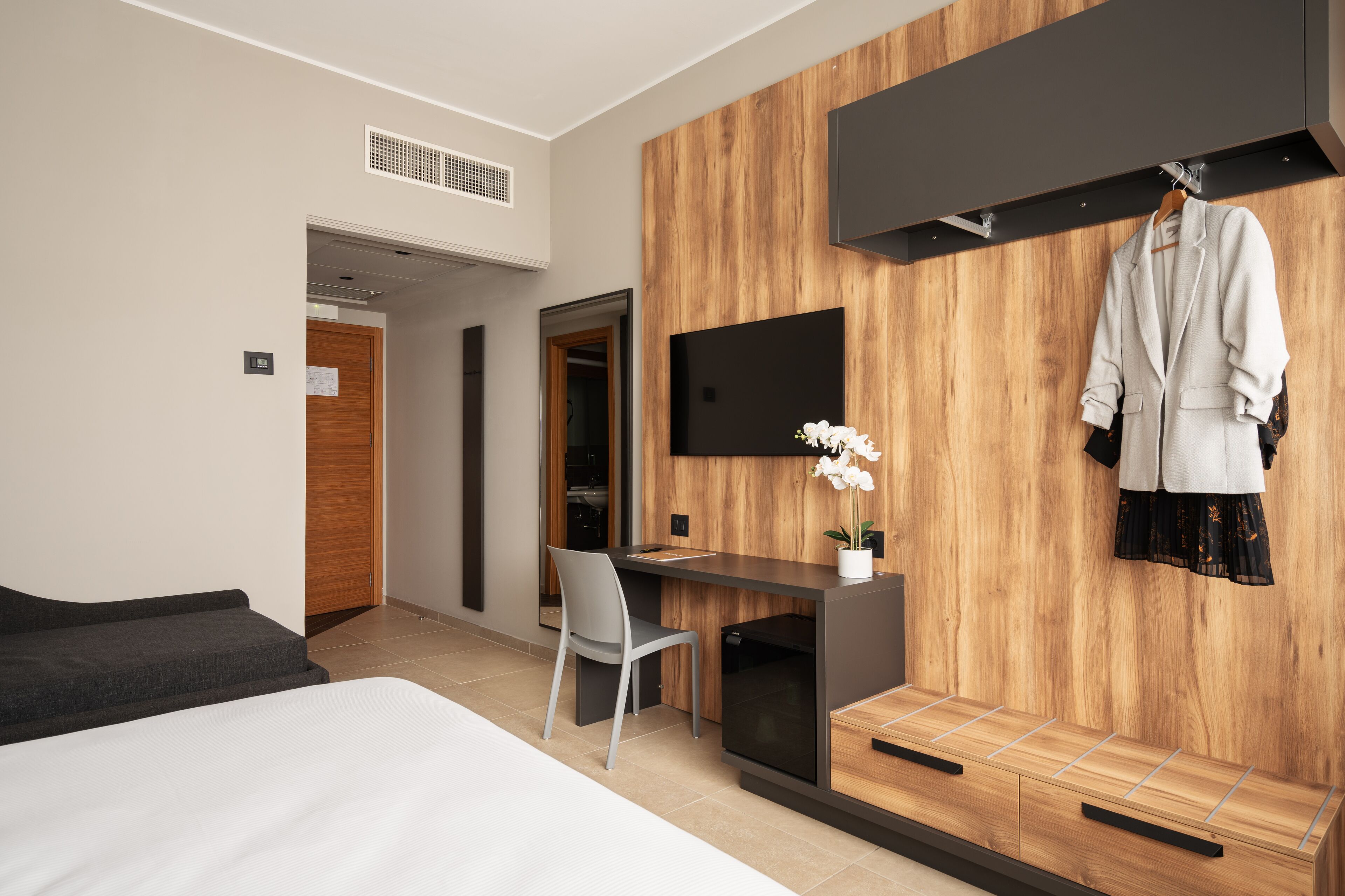 Una habitación de hotel moderna con cama, escritorio, silla, televisor y perchero.